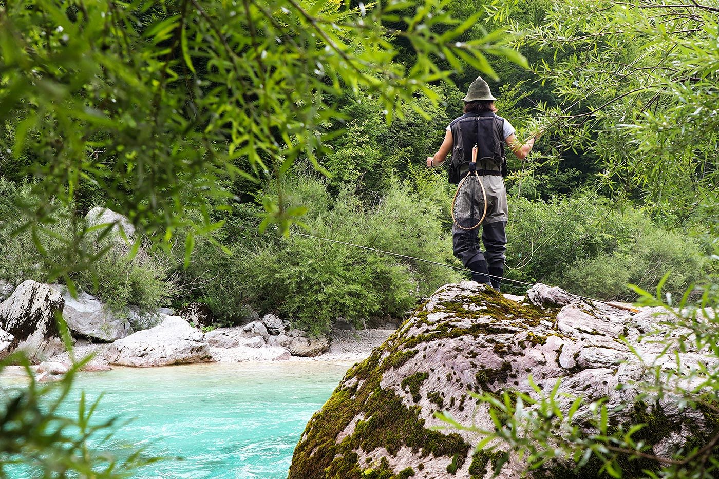 Ein Fliegenfischer auf einem Felsen am smaragdgrünen Fluss Soča